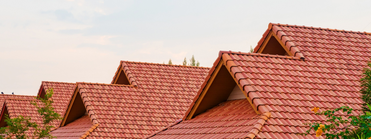 Row of houses with red tiled roofs, expertly crafted from quality roofing materials, stand out against a light sky backdrop.